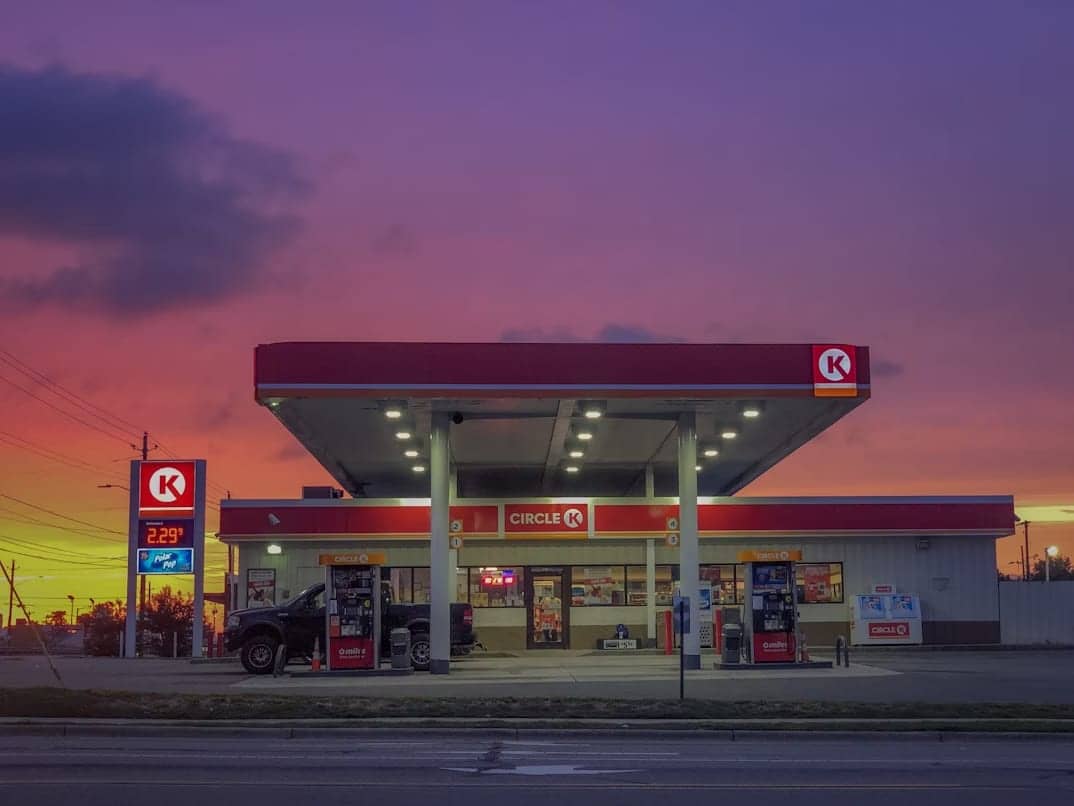 The brightly lit storefront of a Circle K gas station under a colorful sunset sky
