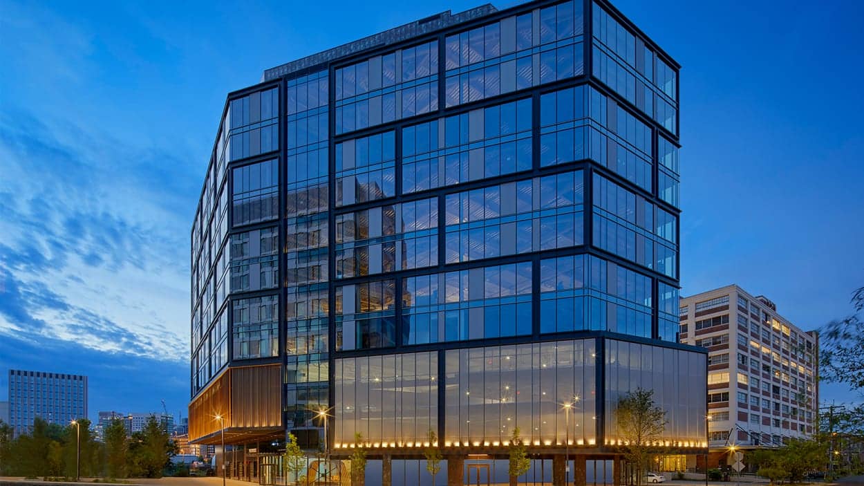 Exterior of a modern commercial office building with a glass facade, illuminated at dusk