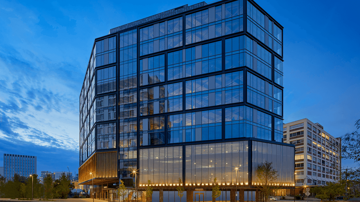 Exterior of a modern commercial office building with a glass facade, illuminated at dusk